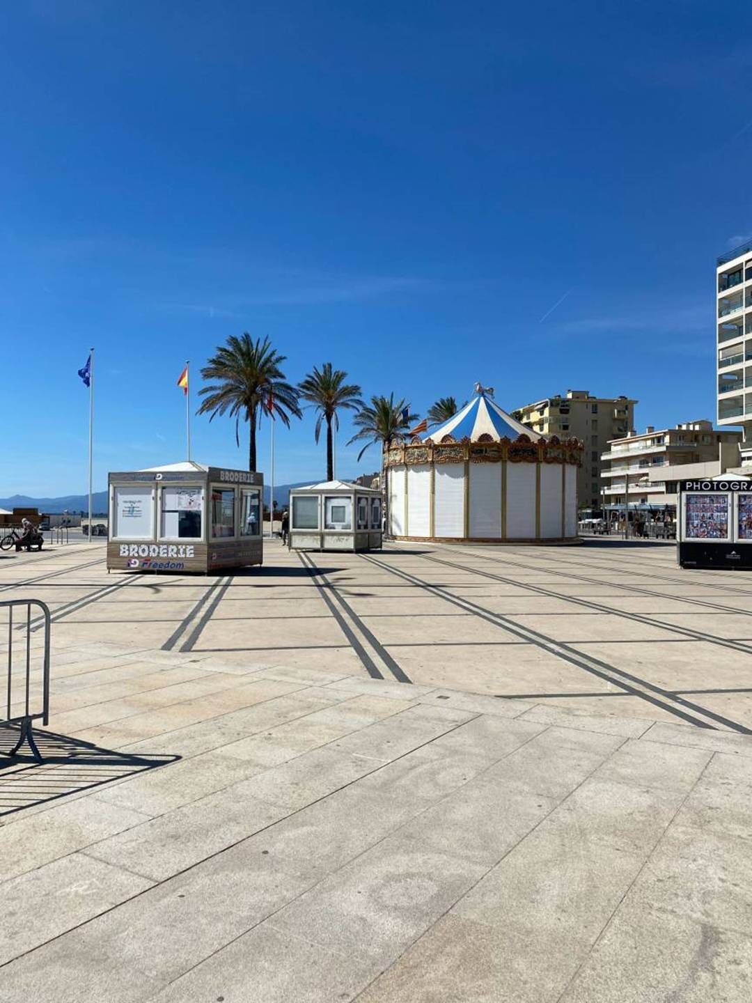 Une place où se trouve un kiosque portant l’inscription « BRODERIE » et une petite structure bleue et blanche en forme de tente.
