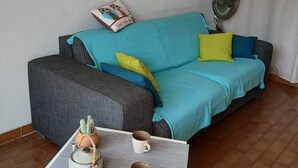 A cozy living room with a grey sofa, a blue and green sofa, a small table with a teapot and cups, a cactus plant, and a painting of a beach scene on the wall. - Studio with Cabin for 4 – Marina View, Beach Just Steps Away, with Elevator Access (CANET PLAGE)