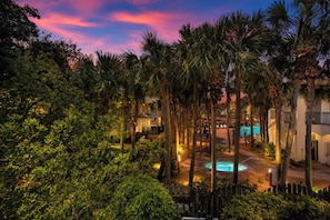 A resort with a swimming pool, palm trees, and a sunset sky.