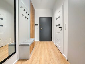 A modern hallway with a bench, a dark door, and a wooden panel wall. - Czysta Urban Living Studio (Wrocław)