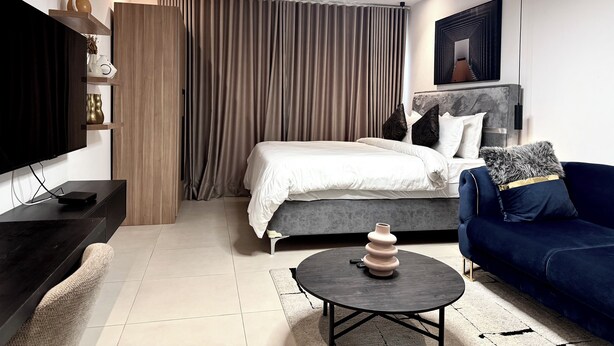 A modern hotel room with a bed, a sofa, a TV, and a coffee table. - Luxury studio pool/gym in east legon at Belrose (Accra)