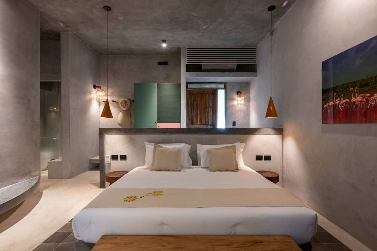 A modern bedroom with a large bed, two bedside tables, a wooden bench, a large window, and a painting of flamingos.