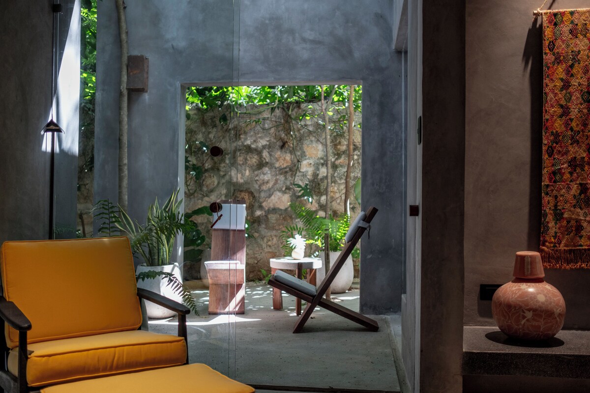Un intérieur moderne avec un canapé jaune, une chaise en bois, une petite table et un vase décoratif.