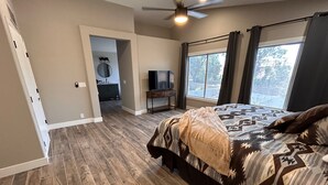 A bedroom with a large bed, a ceiling fan, and a view of the outdoors through a window.