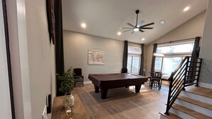 A spacious room with a pool table, a ceiling fan, and a staircase leading to an upper level.