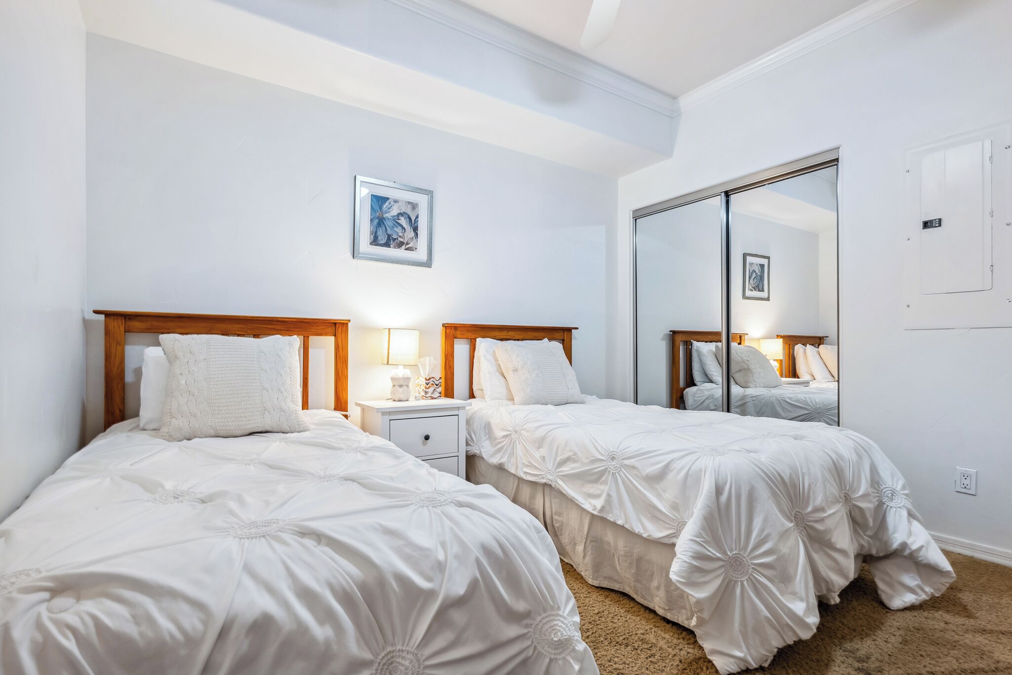 Habitación de hotel con dos camas, una mesita de noche con lámpara, un espejo grande y un cuadro en la pared.