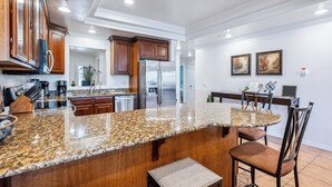 A modern kitchen with granite countertops, wooden cabinets, stainless steel appliances, and a dining area with a table and chairs. -  3 BDR Riverfront Resort w/pool, spa, dock & launch! (Bullhead City)