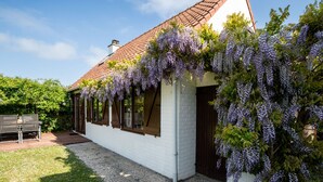 Een wit gebouw met een dak van rode tegels, overwoekerd met paarse wisteria.