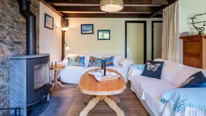 Een gezellige woonkamer met een stenen muur, een open haard, een houten tafel, een bank en een hanglamp.