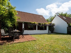 Una casa con techo de tejas, fachada blanca y terraza de madera.