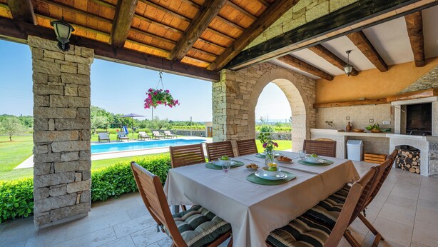 Un espacio de comedor al aire libre con pilares de piedra, una piscina y vistas al campo.