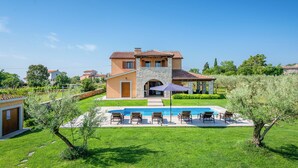 Una casa de dos pisos con fachada de piedra, piscina y mobiliario exterior.