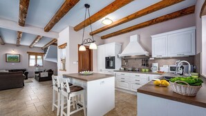 Una cocina moderna con armarios blancos, una isla central y una zona de comedor con un sofá marrón y sillas blancas.