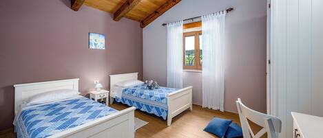 A bedroom with two beds, a wooden ceiling, a window with curtains, and a white wardrobe.