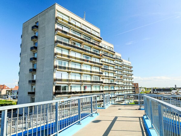 A multi-story residential building with balconies, a pedestrian bridge, and a clear sky.