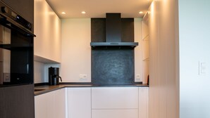 Una cocina moderna con gabinetes blancos, una campana extractora negra y una cafetera integrada.