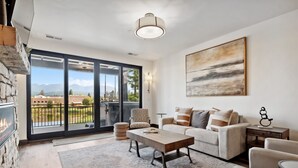 Un salon moderne comprenant un canapé, une table basse et des fauteuils, une cheminée et une grande fenêtre donnant sur un paysage montagneux.