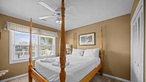 A four-poster bed with a ceiling fan, a window with blinds, and a framed picture on the wall.