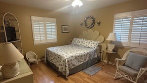 A bedroom with a bed, a ceiling fan, a window with blinds, a wicker chair, and a lamp. - Pet friendly Spacious townhome, quiet neighborhood with pool, 1/2 mile to beach (St. Simons Island)