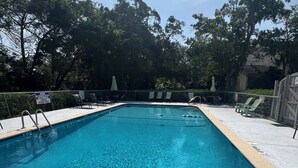A rectangular swimming pool with clear blue water, surrounded by a tiled deck and a metal fence. - Pet friendly Spacious townhome, quiet neighborhood with pool, 1/2 mile to beach (St. Simons Island)