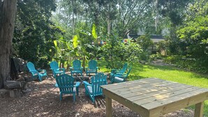 A wooden table and six blue Adirondack chairs arranged in a circle, surrounded by a garden with various plants and trees. - Pet friendly Spacious townhome, quiet neighborhood with pool, 1/2 mile to beach (St. Simons Island)