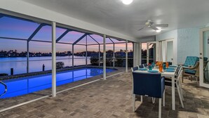 A covered outdoor area with a pool, dining table, chairs, and a ceiling fan.