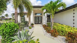 A modern house with a paved pathway leading to the front door, surrounded by various plants and shrubs. - Canal Views & Private Pool - Nirvana on Niagara - Roelens Vacations (Cape Coral)