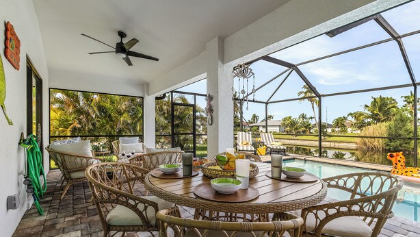 A covered outdoor dining area with wicker furniture, a pool, and a view of the surrounding landscape. - Canal Views & Private Pool - Nirvana on Niagara - Roelens Vacations (Cape Coral)