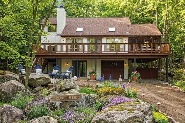 A two-story house with a balcony, a sign reading 'Hideout Retreat,' and outdoor seating. - FALL HIDEOUT 3BR RETREAT•BIG DECK,GAME RM, FIREPIT,FIREPLACE•6BIKES•GOLF•FARMS (Lake Ariel)
