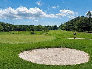 Ein Golfplatz mit einem Bunker, Bäumen und blauem Himmel.