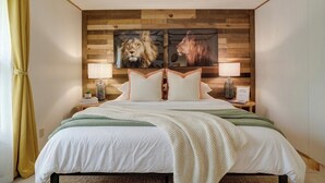 Ein Schlafzimmer mit einem hölzernen Kopfende, einem Bett mit weißer Bettwäsche, zwei Wandlampen und einem Fenster mit gelben Vorhängen.