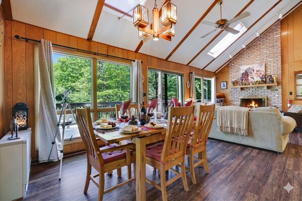 A wooden interior with a dining table, chairs, a fireplace, and large windows. - FALL HIDEOUT 3BR RETREAT•BIG DECK,GAME RM, FIREPIT,FIREPLACE•6BIKES•GOLF•FARMS (Lake Ariel)