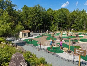 Ein Minigolfplatz mit einem Holzschild, auf dem 'Willkommen! Viel Spaß!' steht.