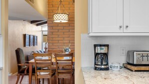 A dining area with a wooden table and chairs, a hanging light fixture, and a brick wall.