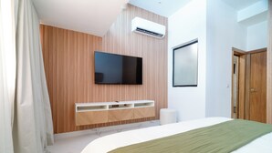 Ein modernes Schlafzimmer mit einem Bett, einem an der Wand befestigten Fernseher, einer Holzpaneelwand und einer weißen Decke.