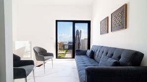 Ein modernes Wohnzimmer mit einem grauen Sofa, zwei Sesseln und einer großen Schiebeglastür, die zu einem Außenbereich führt.
