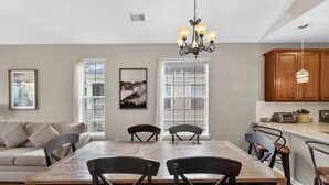 A dining area with a wooden table and chairs, a chandelier, and a kitchen with wooden cabinets and a countertop. - Myrtle Beach Bliss | Golf, Beach & Beautiful Views | RO 52I (Myrtle Beach)