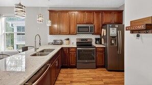 A modern kitchen with wooden cabinets, stainless steel appliances, a granite countertop, and pendant lighting. - Myrtle Beach Bliss | Golf, Beach & Beautiful Views | RO 52I (Myrtle Beach)