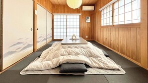 A traditional Japanese-style room with tatami flooring, a futon bed, sliding doors, and a shoji screen. - Spacious Traditional Japanese house by Restavio (Ozu, Kikuchi District)