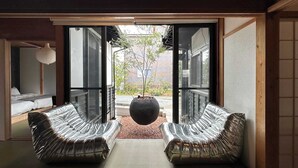 A modern interior with a sliding glass door leading to a garden. Inside, there are two leather sofas facing the door, a tatami mat floor, and a hanging light fixture. - Spacious Traditional Japanese house by Restavio (Ozu, Kikuchi District)
