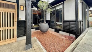 A modern building with a wooden entrance, a large potted plant, and a gravel area. - Spacious Traditional Japanese house by Restavio (Ozu, Kikuchi District)
