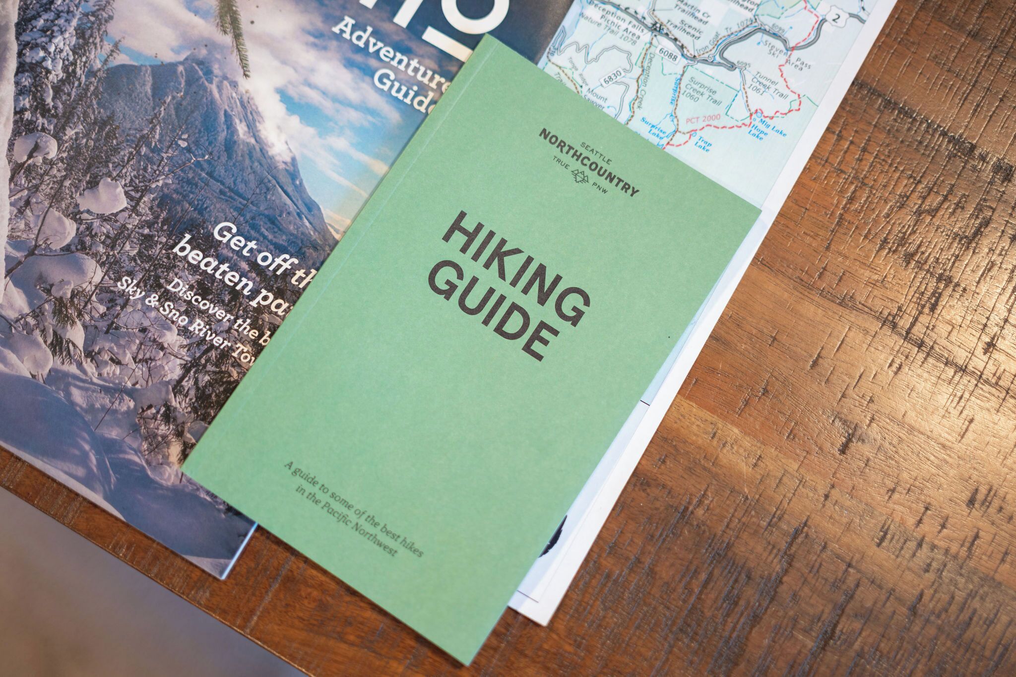 Un livre vert intitulé « Guide de randonnée » est posé sur une surface en bois, à côté d’autres documents imprimés.