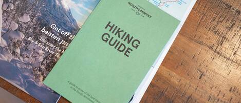 Un livre vert intitulé « Guide de randonnée » est posé sur une surface en bois, à côté d’autres documents imprimés.