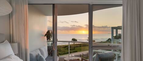Un dormitorio con un ventanal que da a un balcón con vista al atardecer.
