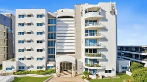 A modern multi-story hotel with a central courtyard, balconies, and a well-maintained lawn. - 1BR Beachfront Retreat ~ Azure Beachfront Bliss (Palm Beach)