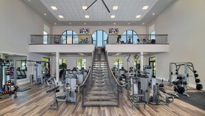 A spacious gym with a central staircase, various exercise machines, and a second-floor balcony with outdoor views. - Fabulous 3-bedroom house with private pool and endless amenities in Estero (Estero)