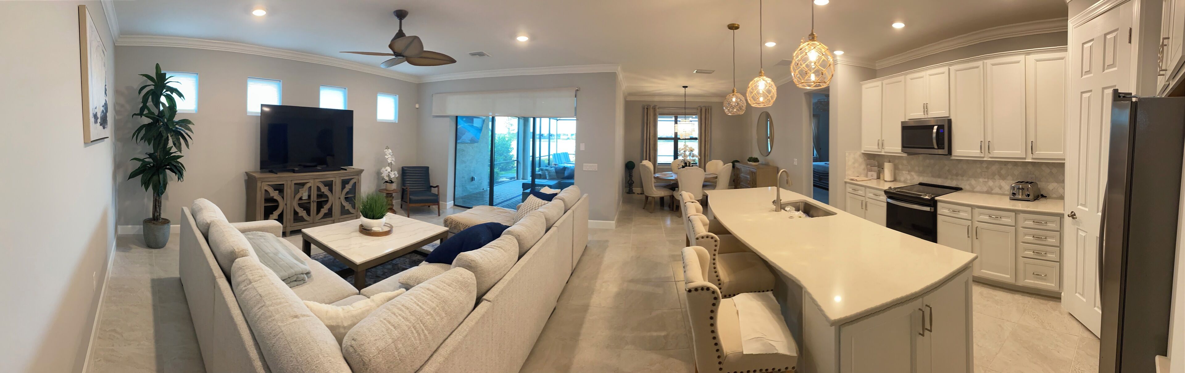 A modern kitchen with white cabinets, a large island, and a dining area with a sofa and chairs.