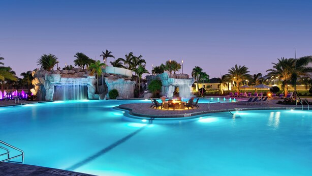 A large outdoor swimming pool with a waterfall feature, lounge chairs, and palm trees. - Fabulous 3-bedroom house with private pool and endless amenities in Estero (Estero)
