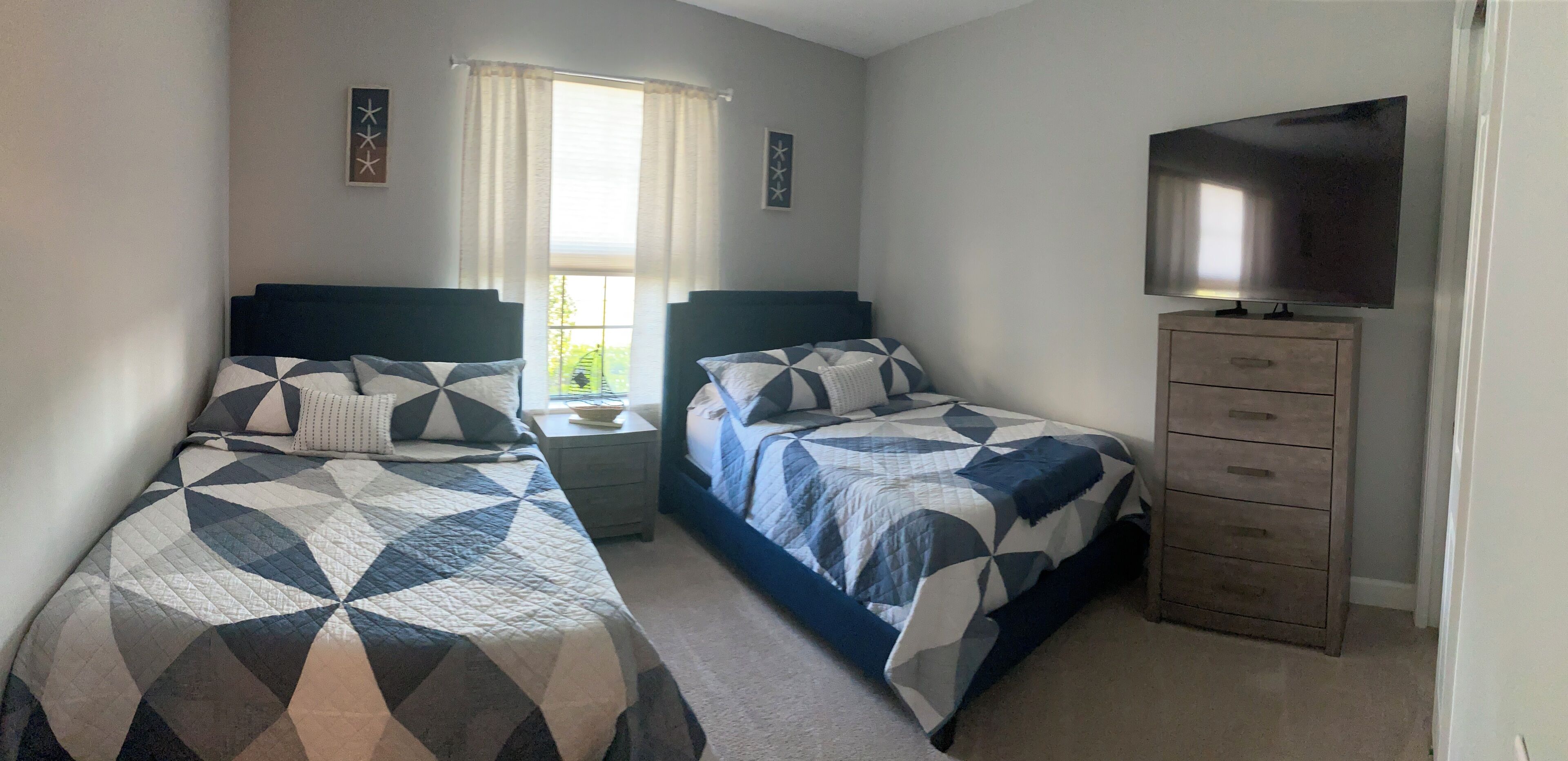 Un dormitorio con dos camas, televisor, cómoda y ventana con cortinas.