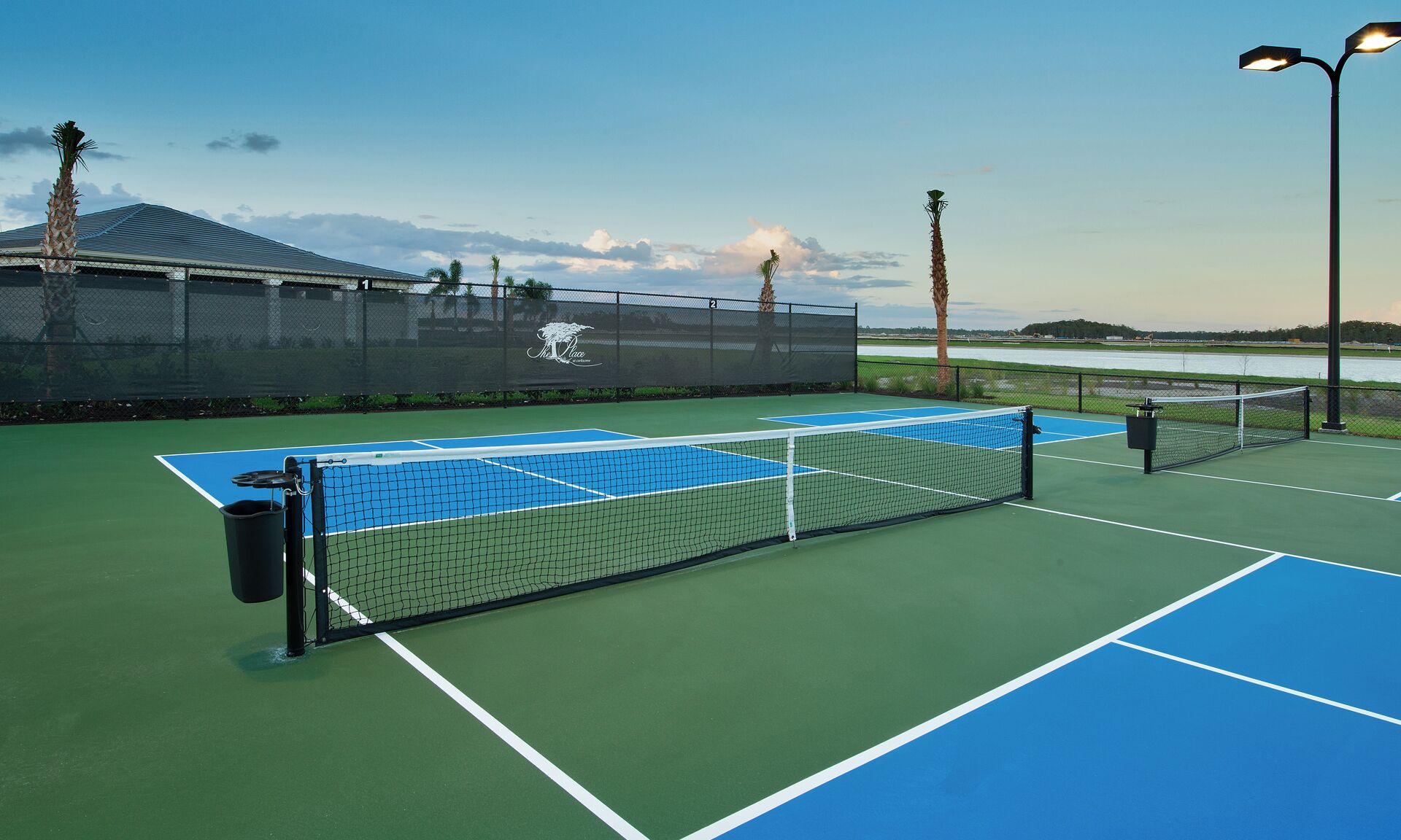 Un court de tennis avec un filet, entouré d’une clôture, et un bâtiment avec un logo en arrière-plan.